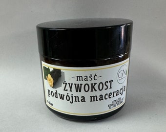 May include: A brown glass jar with a black lid containing a cream or ointment. The label reads "maść - żywokost podwójna maceracja" and "GN Gabinet" with a small green leaf logo. The jar is 60 ml.