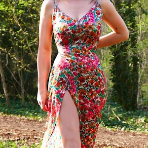 Peut inclure: Robe à imprimé floral avec décolleté en V et fines bretelles. La robe présente une fente haute sur le côté gauche, mettant en valeur un motif vibrant de fleurs rouges, oranges et roses sur fond vert. La robe est en tissu léger.