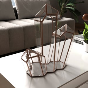 May include: A set of three geometric glass terrariums with a copper frame. The terrariums are shaped like crystals and are arranged in a cluster.