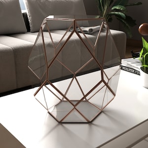 May include: A geometric glass terrarium with a copper frame. The terrarium is sitting on a white table.