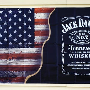 Può includere: Un banner con il design della bandiera americana a sinistra e un'etichetta di whisky Jack Daniel's a destra. La bandiera ha un aspetto di venatura del legno invecchiato. L'etichetta del whisky è nera con testo bianco.