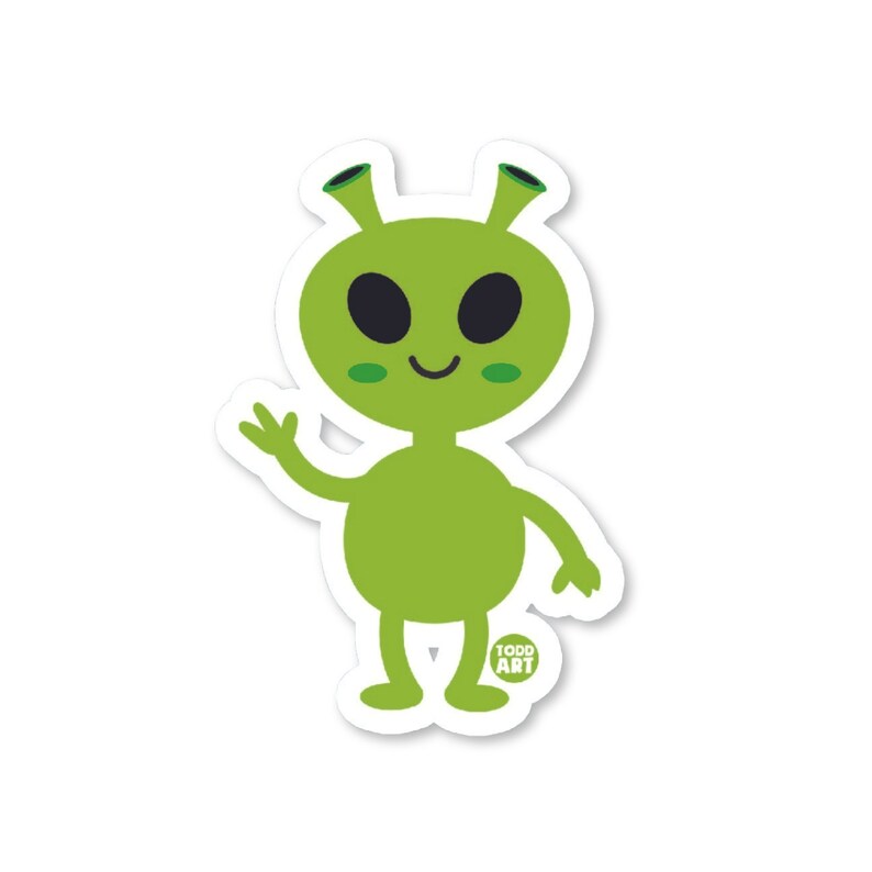 May include: A green alien sticker with a friendly expression, waving one hand. The alien has large black eyes, small green cheek accents, and antenna-like features. The sticker has a white border and the text "TODD ART" in a small circle.