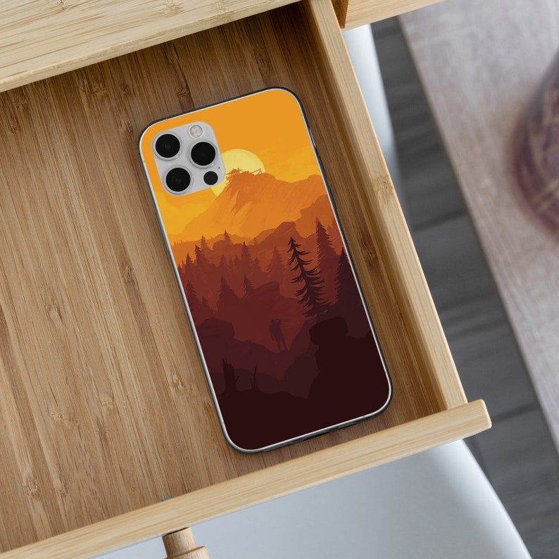May include: A phone case with a sunset scene over a mountain range and forest. The case is white with a colorful design.