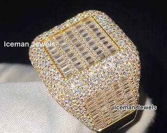 May include: A gold ring with a large square-shaped center stone surrounded by smaller stones. The ring is set with baguette-cut diamonds and round brilliant-cut diamonds.