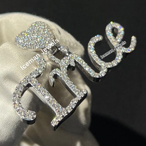 May include: A diamond-encrusted pendant necklace featuring the word "Alice" spelled out in cursive. The pendant also includes a small heart charm. The necklace is made by Iceman Jewels.