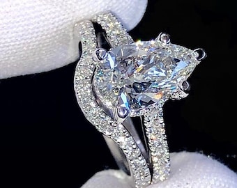 May include: A pear-shaped diamond engagement ring set with a pave band and a matching wedding band. The ring is set in white gold and features a large, sparkling diamond.