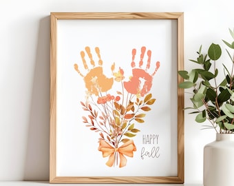 Könnte beinhalten: Gerahmter Druck mit orangefarbenen und gelben Handabdrücken über einem Strauß Herbstlaub und einer Schleife. Die Worte "HAPPY fall" sind in einer Schriftart geschrieben. Der Rahmen ist aus hellem Holz.