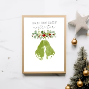 May include: A framed print with a gold border features green footprints below a floral arrangement and the text "I love you from my head to my mistle-toes." The print is a festive holiday decoration.