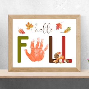 May include: A framed print with the words "hello FALL" in a whimsical design. The letter "F" is green, the handprint is orange, and the letter "L" is red. Autumn leaves and illustrations of mushrooms and hedgehogs complete the fall theme.