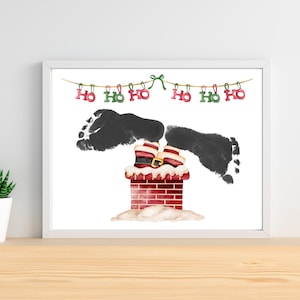 Peut inclure: Impression encadrée sur le thème de Noël. Des empreintes de pieds noires représentent les jambes et les pieds du Père Noël sortant d'une cheminée en briques. Les bottes du Père Noël sont visibles. Les mots "Ho Ho Ho" sont en haut.