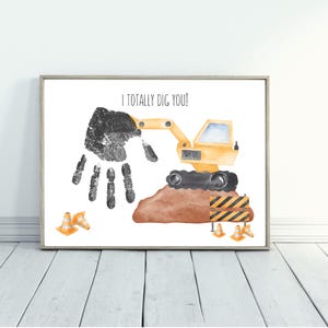 May include: Framed print featuring a black handprint and a yellow excavator. The text "I TOTALLY DIG YOU!" is above the handprint. Construction cones and a brown mound of dirt are also included.