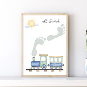 Könnte beinhalten: Gerahmter Druck mit einer Aquarellillustration eines blau-grünen Zuges, Fußabdrücken und einer Sonne. Der Text "all aboard" ist kursiv geschrieben. Die Fußabdrücke sind hellgrau. Der Rahmen ist aus Holz.