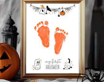 Puede incluir: Una impresión enmarcada con huellas de pies naranjas e ilustraciones de Halloween. La impresión incluye una pancarta con un fantasma, un murciélago y una calabaza, y el texto "my first HALLOWEEN". El marco es dorado.