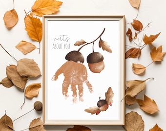 May include: A framed print with the text "Nuts About You" and a handprint design resembling acorns. The artwork features brown and tan colors, with additional acorn illustrations and autumn leaves scattered around the frame.