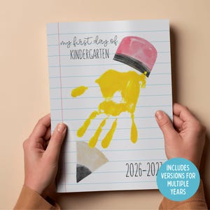 Peut inclure: Une page de carnet avec le texte "my first day of KINDERGARTEN" et une empreinte de main jaune en forme de crayon. La gomme du crayon est rose et noire, et la pointe du crayon est grise. Le carnet indique également les années 2026-2027.