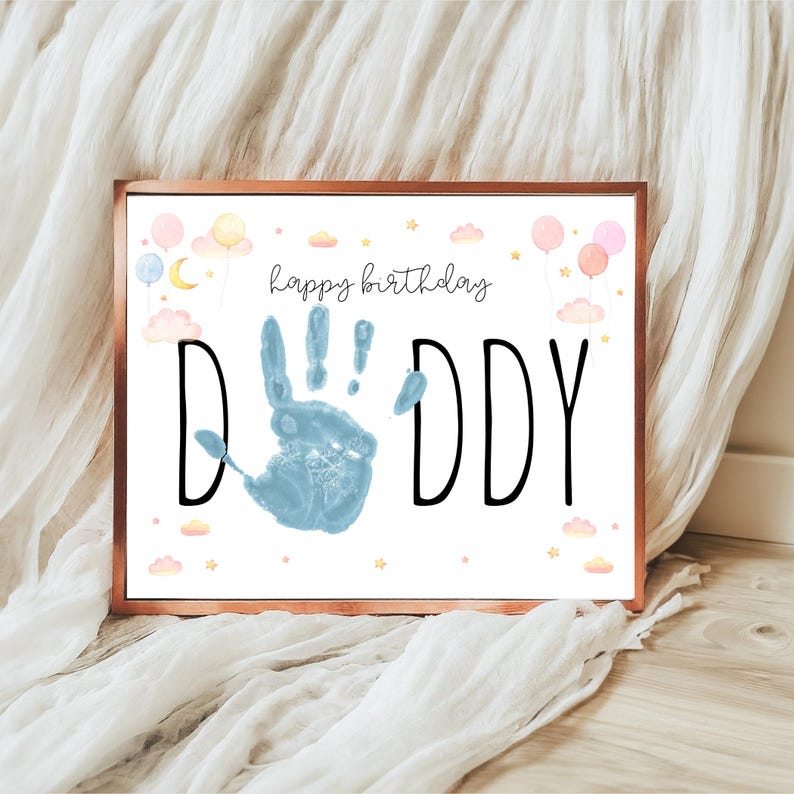 Pu&ograve; includere: Stampa incorniciata con bordo color rame. La stampa presenta le parole "happy birthday DADDY" con un'impronta blu al centro. Palloncini, nuvole e stelle dai colori pastello decorano la parte superiore e inferiore.