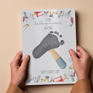 May include: A Father's Day card featuring a gray footprint forming the head of a hammer. The hammer handle is beige and blue. The card reads "I love building memories with you!" and "Happy Father's Day!" with tool illustrations.