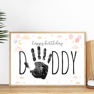 Pu&ograve; includere: Stampa incorniciata con le parole "happy birthday DADDY" in nero. Un'impronta di mano nera &egrave; al centro. La stampa &egrave; decorata con palloncini, nuvole e stelle ad acquerello in colori pastello.