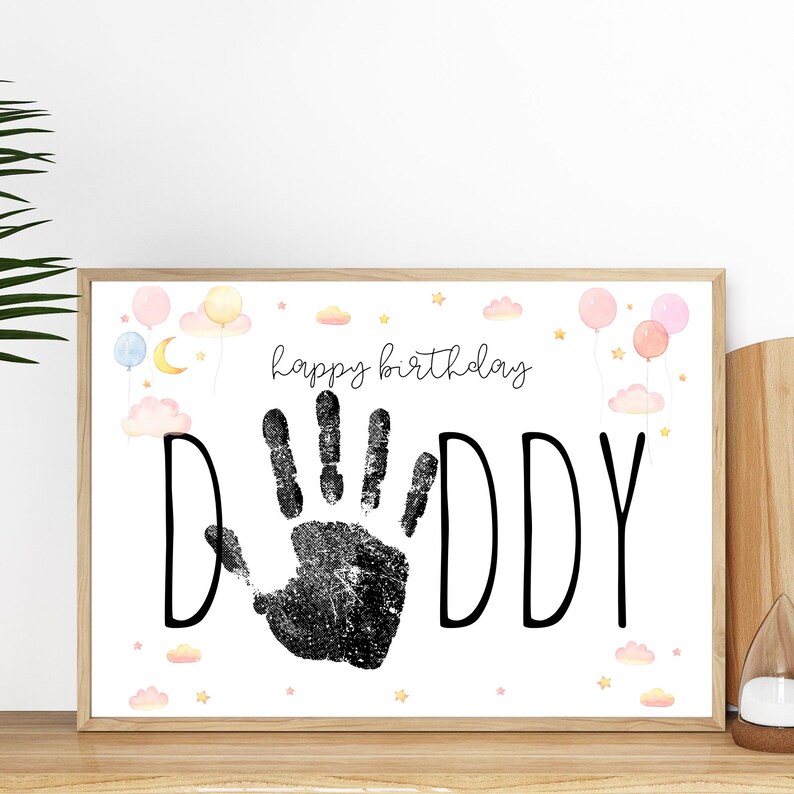 Pu&ograve; includere: Stampa incorniciata con le parole "happy birthday DADDY" in nero. Un'impronta di mano nera &egrave; al centro. La stampa &egrave; decorata con palloncini, nuvole e stelle ad acquerello in colori pastello.