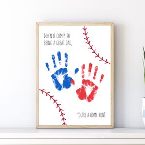 May include: A framed print on a white background featuring a blue handprint and a red handprint. The text reads, "WHEN IT COMES TO BEING A GREAT DAD, YOU'RE A HOME RUN!" Red baseball stitching graphics are positioned in the top right and bottom left corners.