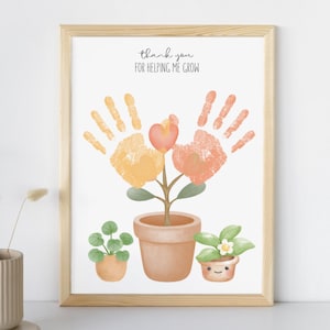 May include: A framed print featuring a handprint flower design with the text "thank you FOR HELPING ME GROW." The artwork includes a potted plant and two smaller potted plants. The frame is made of light-colored wood.