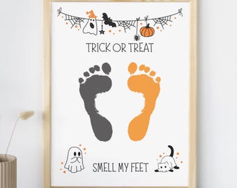 May include: A framed Halloween-themed print with a light wood frame. The print features the text "TRICK OR TREAT" above two footprints, one gray and one orange. Below the footprints is the text "SMELL MY FEET". Decorative Halloween elements are included.