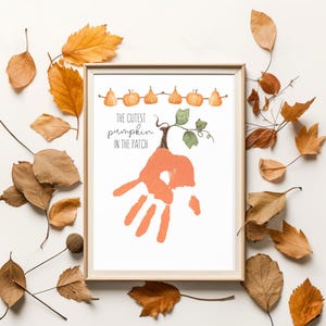 May include: A framed print featuring a handprint shaped like a pumpkin with the text "The Cutest Pumpkin in the Patch." The artwork is surrounded by autumn leaves in shades of brown and orange, creating a seasonal theme.