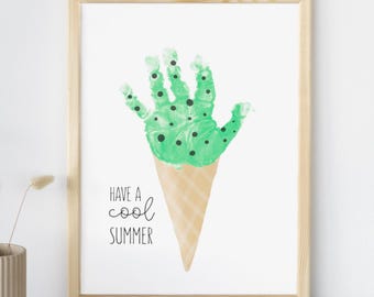 May include: A framed print featuring a handprint in green paint with black dots, shaped like ice cream on a cone. The text "Have a cool summer" is below the ice cream. The frame is made of light brown wood.