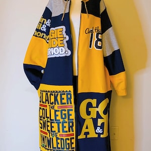 May include: A long, color-blocked zip-up hoodie in navy blue, yellow, and grey. The garment features various graphic prints including the text "THE BLACKER THE COLLEGE THE SWEETER THE KNOWLEDGE," "GIE RIDE RIOD," "And the 18," and "GOAT &."