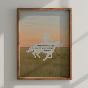 Op de afbeelding: Ingelijst kunstwerk met een silhouet van een ruiter op een paard tegen een zonsondergangachtergrond. Het kunstwerk bevat de tekst "When the time is right, I the Lord will make it happen." in een decoratief lettertype. Het frame is van hout.