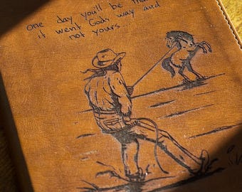 May include: A brown leather journal with a cowboy illustration roping a horse. The journal cover has the handwritten text: "One day you'll be thankful it went Gods way and not yours..."
