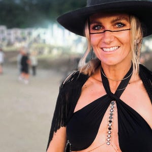 May include: A woman wearing a black halter top with a silver chain and black fringe shawl. She is wearing a black hat and has black eyeliner and a silver nose ring.