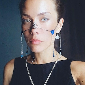May include: A woman wearing a silver nose chain with blue accents and a silver chain necklace with a large circular pendant. She is wearing a black tank top.