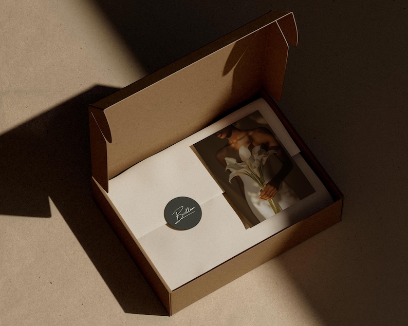Op de afbeelding: Een open bruine kartonnen verzenddoos met daarin een witte envelop verzegeld met een donkergrijze ronde sticker met de witte tekst Britten, naast een rechthoekige print waarop een persoon met een boeket witte lelies is afgebeeld.