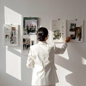 Puede incluir: Un blazer blanco usado por una persona frente a una pared con cuatro carteles rectangulares que presentan fotograf&iacute;as de bodas, arreglos florales y texto. Los carteles est&aacute;n colgados con clips, mostrando varias escenas nupciales.