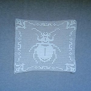 May include: A square, white, crocheted doily featuring a detailed insect design in the center. The doily has a delicate, openwork pattern with a scalloped edge. The insect appears to be a beetle or scarab, adding a touch of nature-inspired decor.