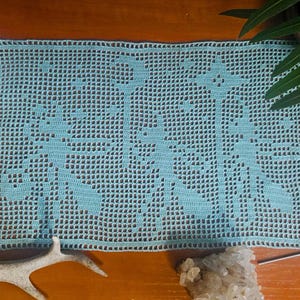 May include: A rectangular, light blue crocheted doily with a floral pattern. The doily is placed on a wooden surface, with a cactus in a white pot, a piece of antler, and a crystal cluster in the background.