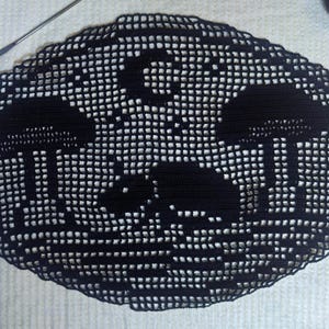 May include: Black, oval-shaped, crocheted doily featuring a mushroom design. The doily is made of a dark yarn and has a scalloped edge. A crochet hook and other craft supplies are visible.