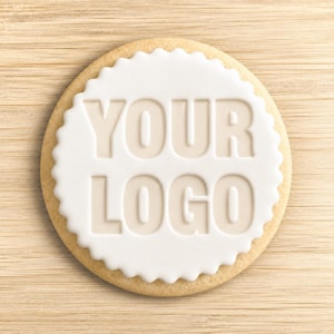Op de afbeelding: Een rond koekje met een geschulpte rand, bedekt met een gladde laag wit glazuur. De woorden YOUR LOGO zijn in het midden van het glazuur gedrukt, wat een verdiept, driedimensionaal effect op het oppervlak van het koekje creëert.