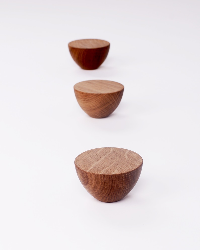 May include: Three wooden, semi-spherical objects in varying shades of brown are arranged vertically against a white background. The objects have a flat top and a rounded base, showcasing the natural wood grain.
