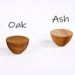 May include: Two wooden, semi-circular objects, one oak and one ash, are displayed against a white background. The oak piece is a darker brown, while the ash is a lighter tan. The word "Oak" is written above the darker piece, and "Ash" above the lighter one.