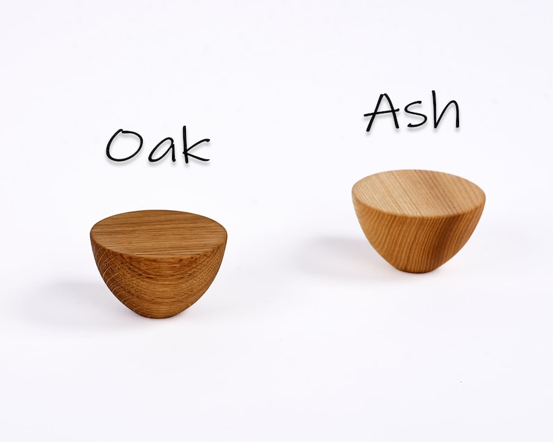 May include: Two wooden, semi-circular objects, one oak and one ash, are displayed against a white background. The oak piece is a darker brown, while the ash is a lighter tan. The word "Oak" is written above the darker piece, and "Ash" above the lighter one.