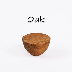 May include: A solid, half-sphere shaped wooden object with a flat top and curved bottom. The wood grain is visible, and the object is a light brown color. The word "Oak" is written above the object in black script.