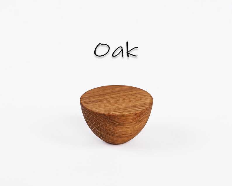 May include: A solid, half-sphere shaped wooden object with a flat top and curved bottom. The wood grain is visible, and the object is a light brown color. The word "Oak" is written above the object in black script.