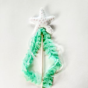 May include: A white felt starfish with pink glitter accents on a wooden stick with a green tulle ribbon.
