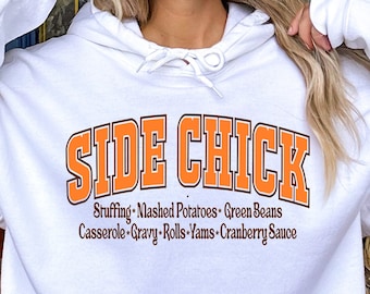 May include: White hoodie with the text "SIDE CHICK" in orange and brown lettering. Below the text are the words "Stuffing, Mashed Potatoes, Green Beans, Casserole, Gravy, Rolls, Yams, Cranberry Sauce."