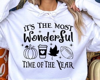 May include: White hoodie with the text "It's the Most Wonderful Time of the Year" and fall-themed graphics. The design includes a pumpkin, coffee cup, leaf, and football. The hoodie is a comfortable, casual style.