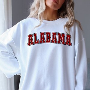 Puede incluir: Sudadera blanca con un gr&aacute;fico "ALABAMA" en rojo y negro.