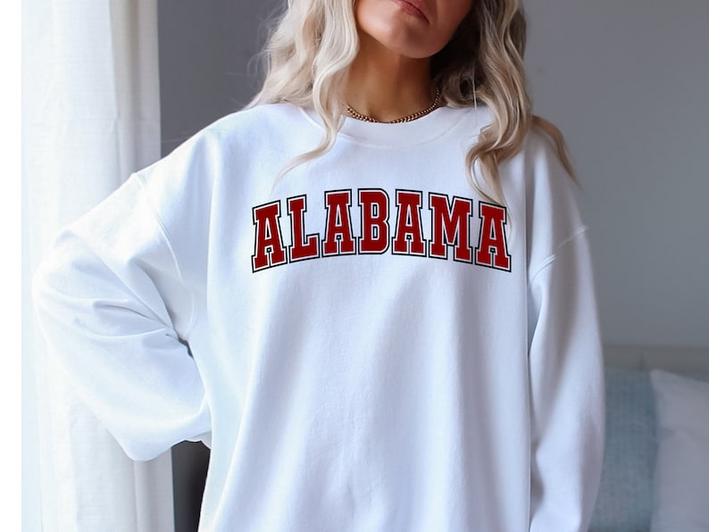 Puede incluir: Sudadera blanca con un gr&aacute;fico "ALABAMA" en rojo y negro.