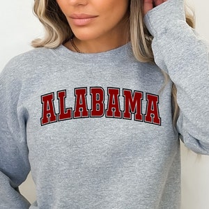 Puede incluir: Una sudadera gris con la palabra "ALABAMA" impresa en rojo en la parte delantera.